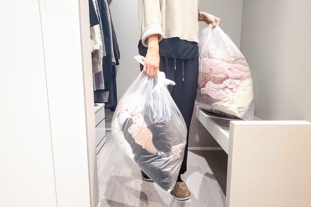 着ない服をゴミ袋に入れて捨てる女性